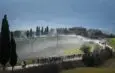 Un peloton de cyclistes sur une route de gravier lors des Strade Bianche en Italie, soulevant de la poussière.