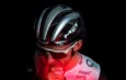 Cycliste portant un casque noir et argent MET et des lunettes blanches, éclairé par une lumière rouge.