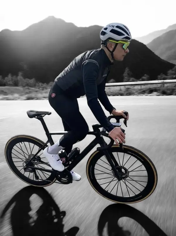 Vue de profil d'un cycliste en tenue noire, avec un paysage de montagne 