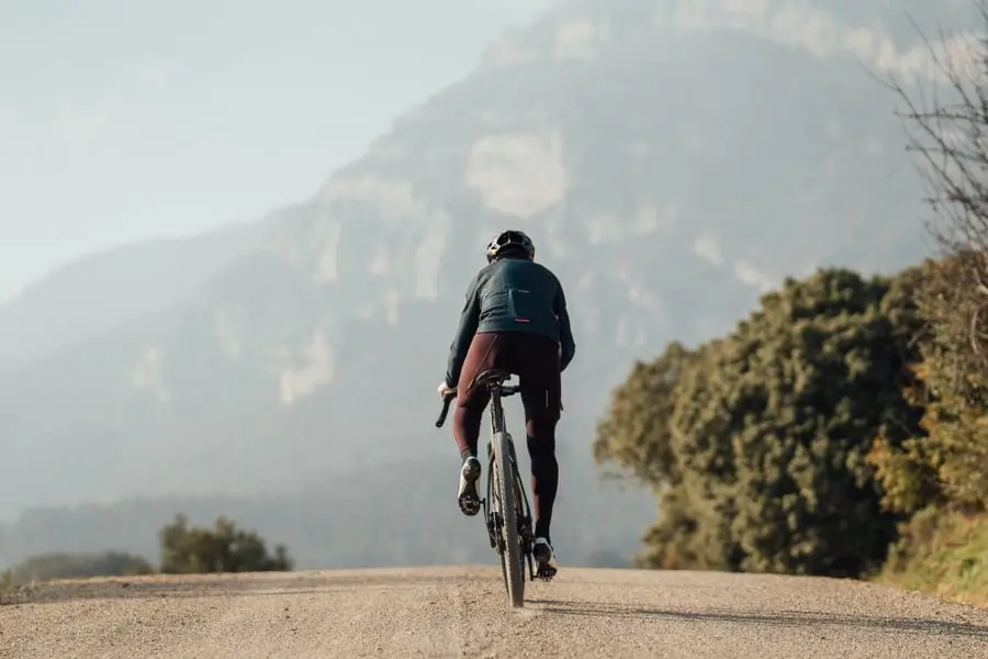 Cycliste sur une route de gravel avec une montagne en arrière plan