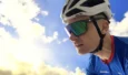 Cycliste portant un casque blanc Kask et des lunettes Adidas, de profil sur fond de ciel nuageux.