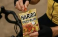 Un cycliste sort un bonbon d'un sachet de Haribo Gold-Bears tenu à la main.