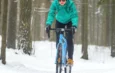 Cycliste en veste verte roulant à vélo sur un sentier forestier enneigé.