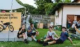 Quatre cyclistes assis sur l'herbe buvant une bière devant un panneau Jeroboam Gravel Series et un vélo.