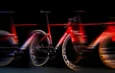 Vélo de route Orbea rouge et noir avec un effet de flou de mouvement sur fond noir.