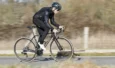 Cycliste casqué habillé de noir roulant sur un vélo de route Cervélo R5 sur une route goudronnée.