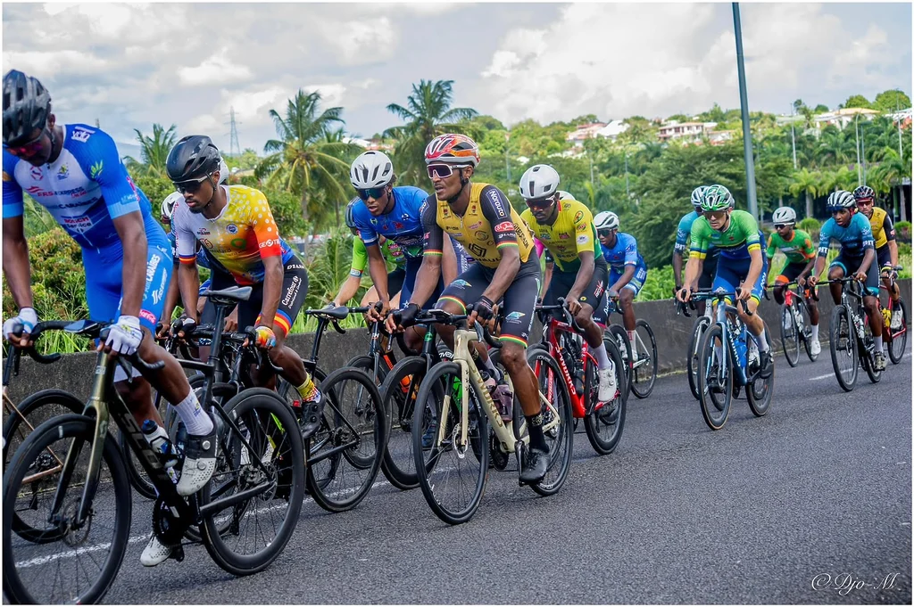 Boris Carène au sein du peloton sur une route de Guadeloupe, entouré des coureurs et du paysage tropical de l’île.