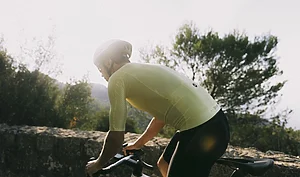 Un cycliste en maillot jaune clair et casque blanc roule sur une route de campagne.