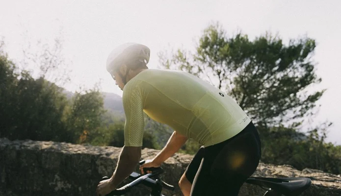 Un cycliste en maillot jaune clair et casque blanc roule sur une route de campagne.