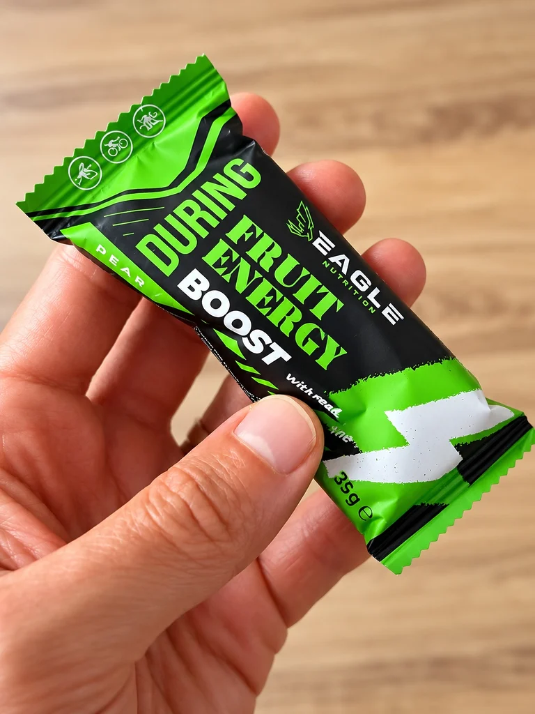 Photographie rapprochée de la barre Eagle Nutrition Fruit Energy BOOST au parfum poire-citron vert. Cette version caféinée associe un apport glucidique destiné à soutenir l'effort à une dose de caféine, susceptible d'agir sur la vigilance et la perception de la fatigue.