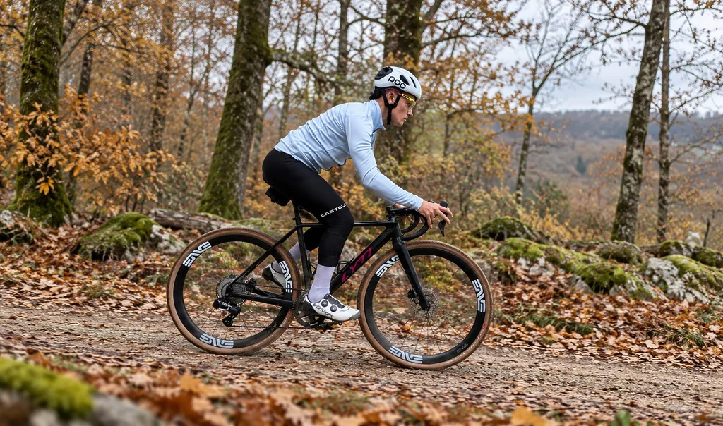 Cycliste en gravel portant la veste Castelli Perfetto 4 Steel Fade avec membrane Polartec AirCore, sur un sentier forestier aux couleurs de l'automne.