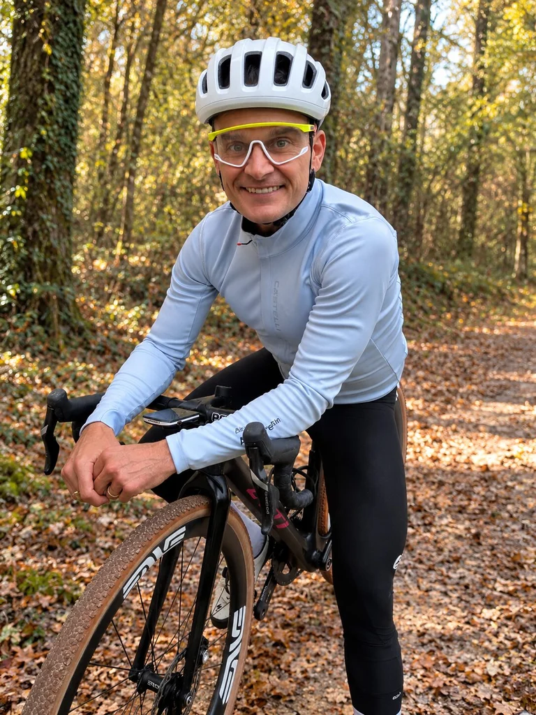 Jeff Tatard souriant, appuyé sur le guidon de son gravel LYTI, avec la veste Castelli Perfetto 4 Steel Fade et sa membrane Polartec AirCore, en forêt automnale.