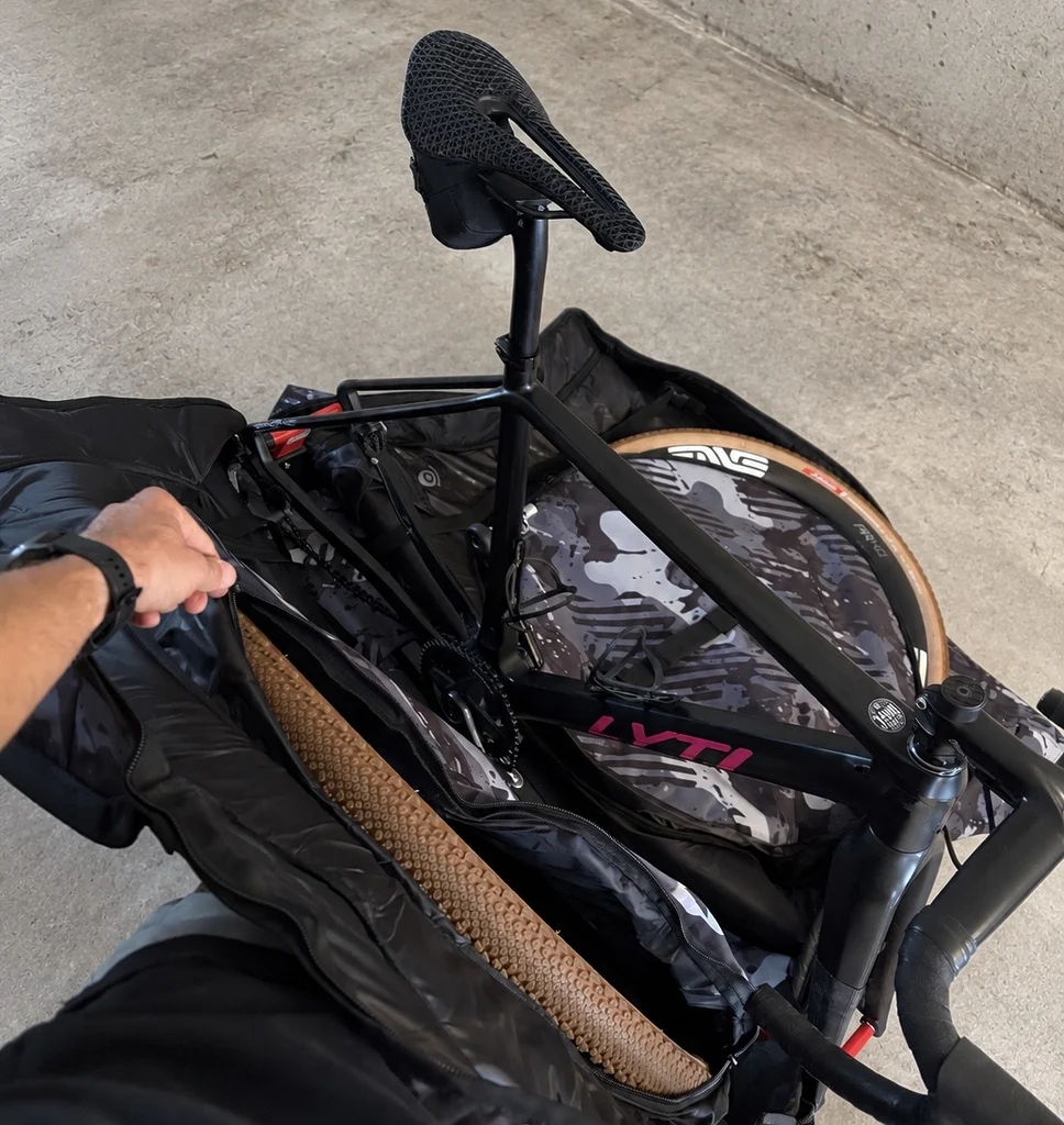 Vue de la housse Scicon Aerocomfort 3.1 Gravel entièrement ouverte avec le vélo Lyti installé sur son support intérieur, les compartiments de roues et la notice illustrée de montage HOW TO PACK.