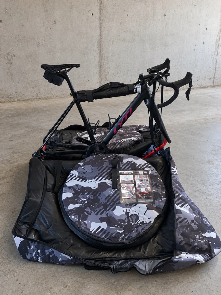 Vue de l'intérieur de la housse Scicon Aerocomfort 3.1 Gravel, montrant une roue de gravel à flancs beiges rangée dans son compartiment de protection, à côté du cadre Lyti.