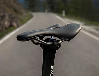 Gros plan sur une selle de vélo SLR montée sur une tige de selle, avec une route en arrière-plan.